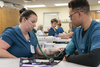 Two CWI students in a medical classroom using blood pressure equipment