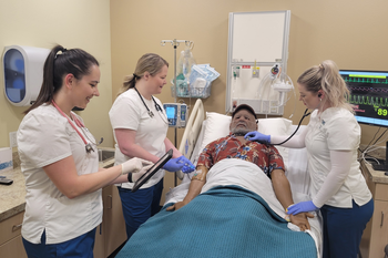 Group of CWI students in scrubs over a mannequin