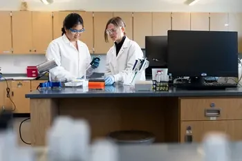 Two CWI students in lab coats and safety glasses in a lab
