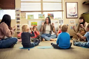 Teachers working with group of young children while sitting in a circle on the floor