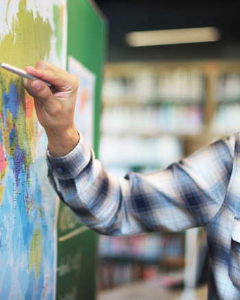 Person with glasses and a flannel pointing at a world map