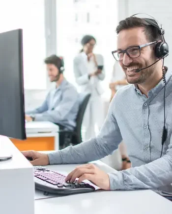 Person with headset in an office smiling at a computer screen