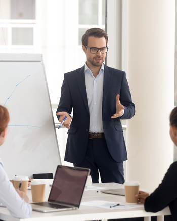 Man standing and giving a presentation in front of a group of people in a meeting