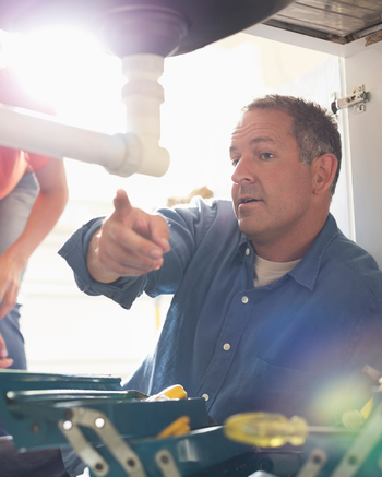 Plumber working under sink pointing out problems to home owners