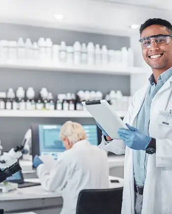 Two pharmasists in a lab and one is looking at the camera