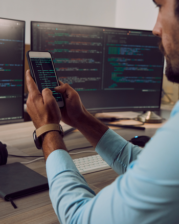 Person holding a phone with coding on it in front of computers with code