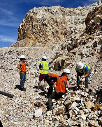People in the field sorting through rocks on cliff side