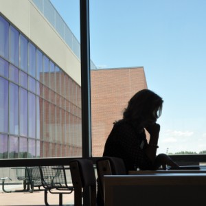 Silhouette of student studying at desk in front of windows.