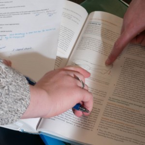 Close up of two people's hands pointing to items in a textbook.