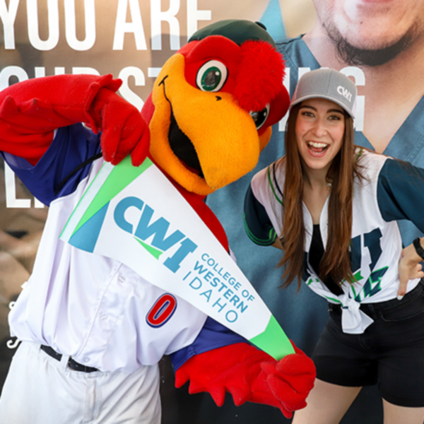 CWI student and mascot smile while holding a CWI pennant at a community event.