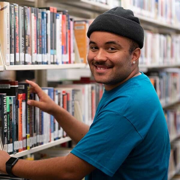 Student in library next to book shelf