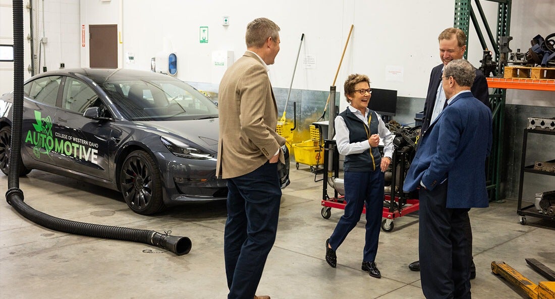 A group of people take a tour of an automobile repair lab at a college.