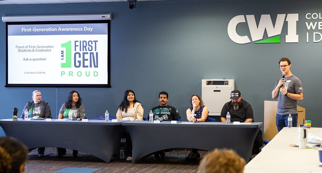 People sit at a table listening to a speaker talk about first-generation college students.