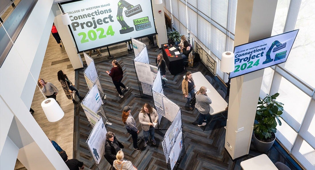 A photo of a student exhibit featuring project posters that line aisle partitions, taken from an elevated platform.