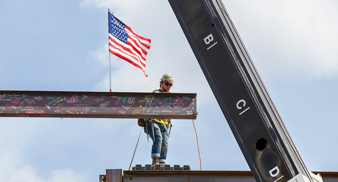A construction worker standing on a steel beam gets ready to place a new beam, covered with signatures, onto a structure.