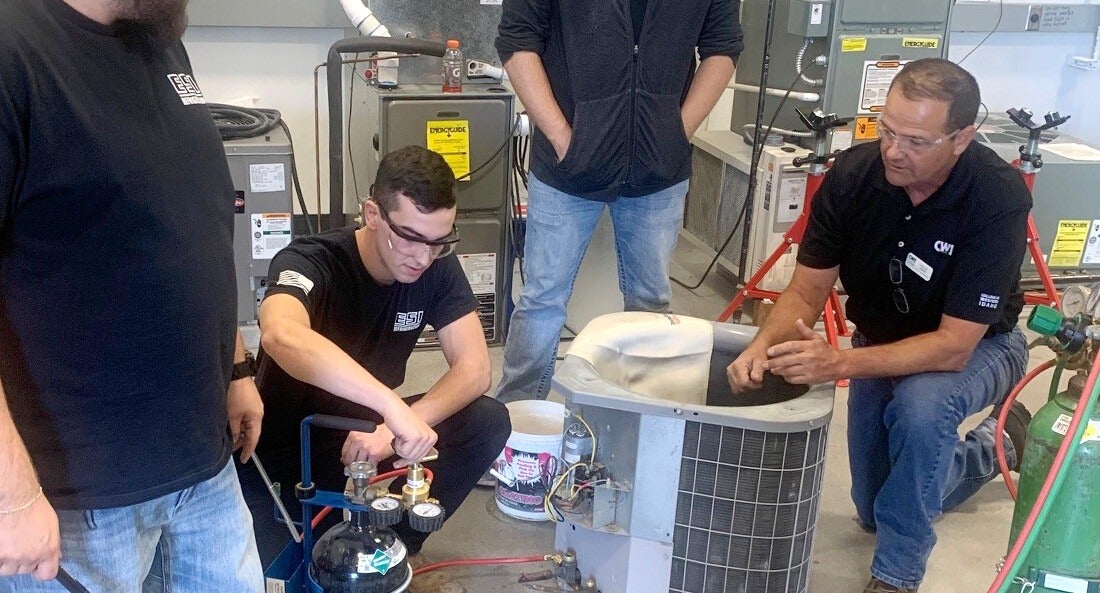 A group of students learn how to repair an air conditioning unit from an instructor.