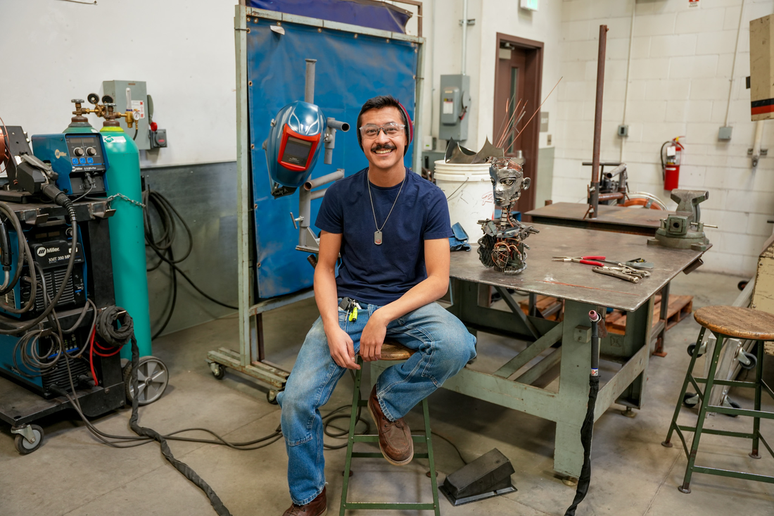 Person sitting on a stool, next to desk and welding tools