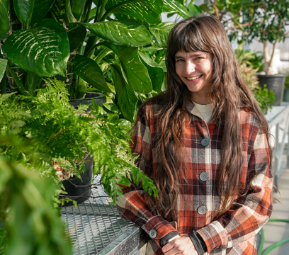 Student stands in greenhouse in front of several plants