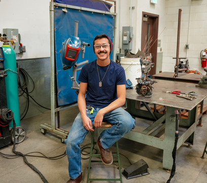 Person sitting on a stool, next to desk and welding tools
